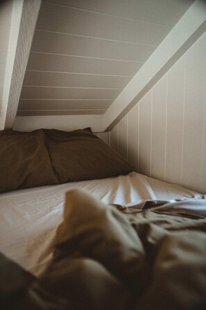 Una litera con colchón y almohadas, techo inclinado y paneles de madera en las paredes.