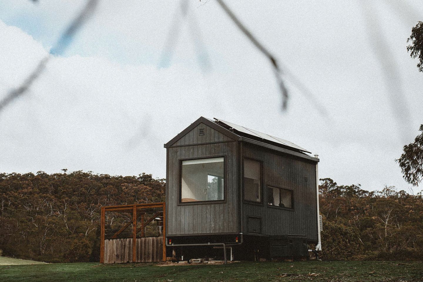 A wooden cabin with a large window, a small porch, and a fenced yard.