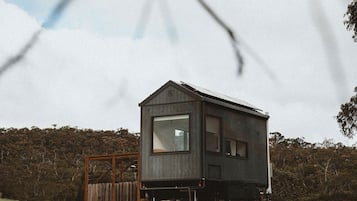 A wooden cabin with a large window, a small porch, and a fenced yard.