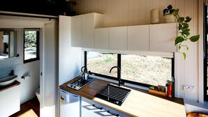 Uma cozinha compacta com fogão embutido, pia e janela com vista para um jardim.
