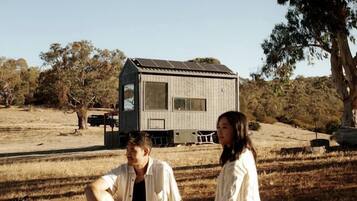 Two people sitting on a blanket outdoors with a small wooden structure in the background.