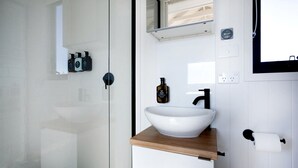 Uma casa de banho moderna com cabine de duche em vidro, uma pia branca com bancada de madeira e um espelho sobre a pia.