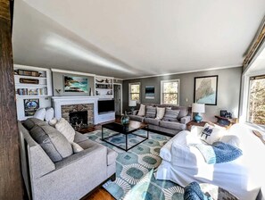 Een woonkamer met een open haard, banken, een salontafel en een boekenkast.