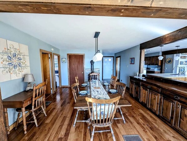 A dining area with a wooden table and chairs, a kitchen with dark wooden cabinets, and a large window.