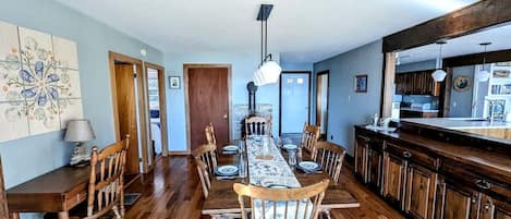 A dining area with a wooden table and chairs, a kitchen with dark wooden cabinets, and a large window.