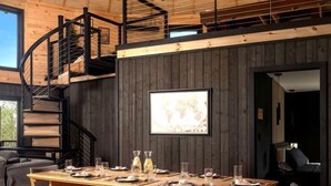 Un coin repas avec une table et des bancs en bois, un escalier en colimaçon et une carte du monde encadrée accrochée au mur.
