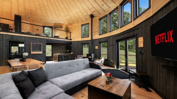 A modern interior with a large gray sectional sofa, a wooden coffee table, and a flat-screen TV mounted on the wall.