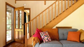 A staircase with wooden railings leading to a room with a grey sofa and a door with glass panels. - Embrace Nature's Warmth: Cozy Glamping Haven Among Drummond's Gum Trees (Drummond)