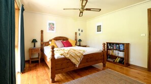 A bedroom with a wooden bed, bedside lamps, a ceiling fan, a bookshelf, and a rug. - Embrace Nature's Warmth: Cozy Glamping Haven Among Drummond's Gum Trees (Drummond)