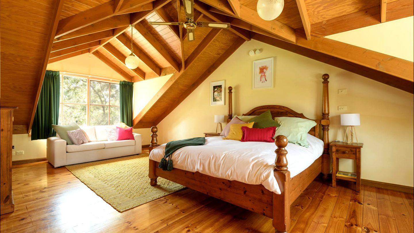 Un dormitorio con techo de madera, una cama con cabecera de madera, una mesita de noche y una ventana con cortinas.