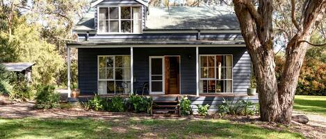 A two-story house with a porch, large windows, and a tree in the foreground.