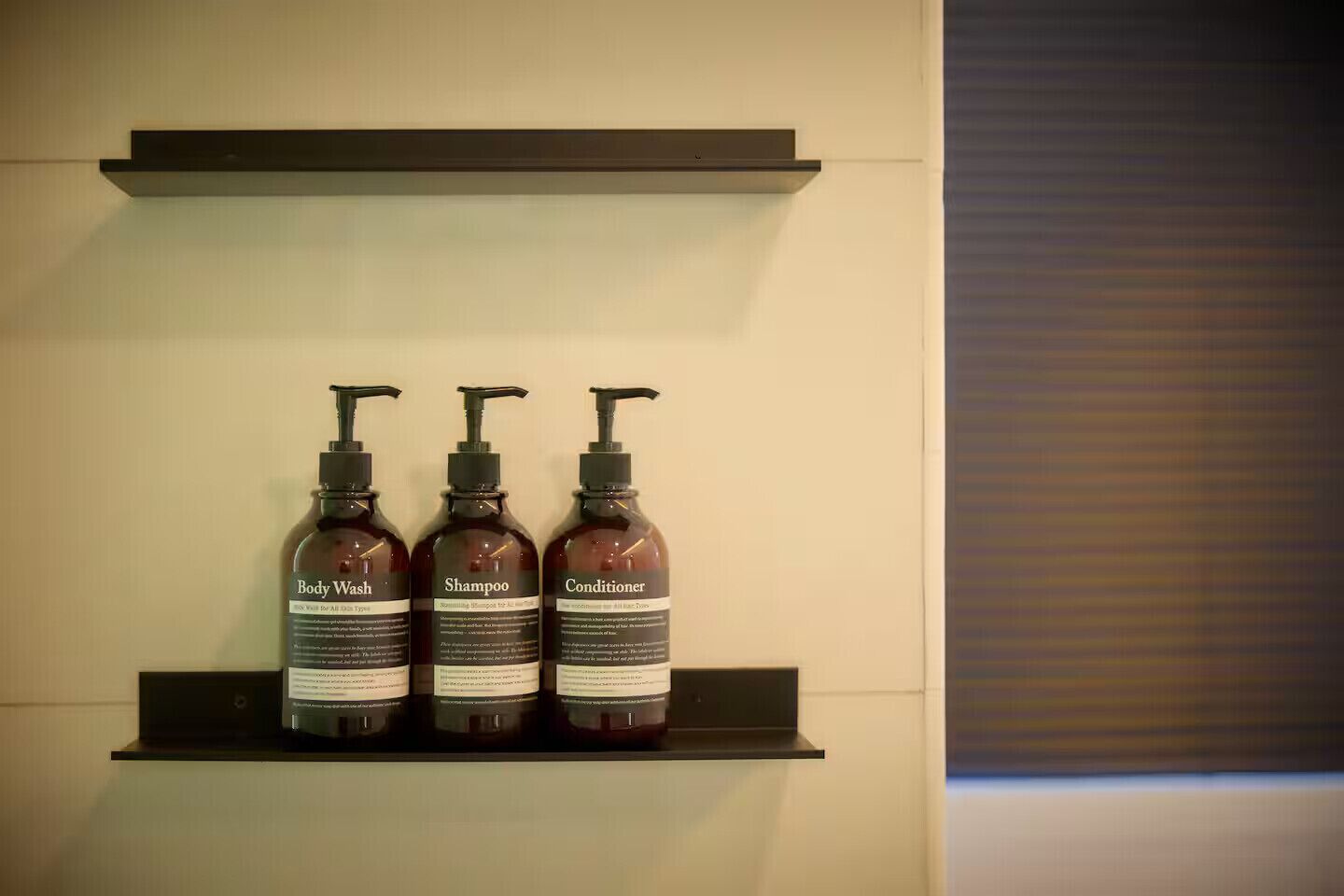 A shelf with three bottles of body wash, shampoo, and conditioner.