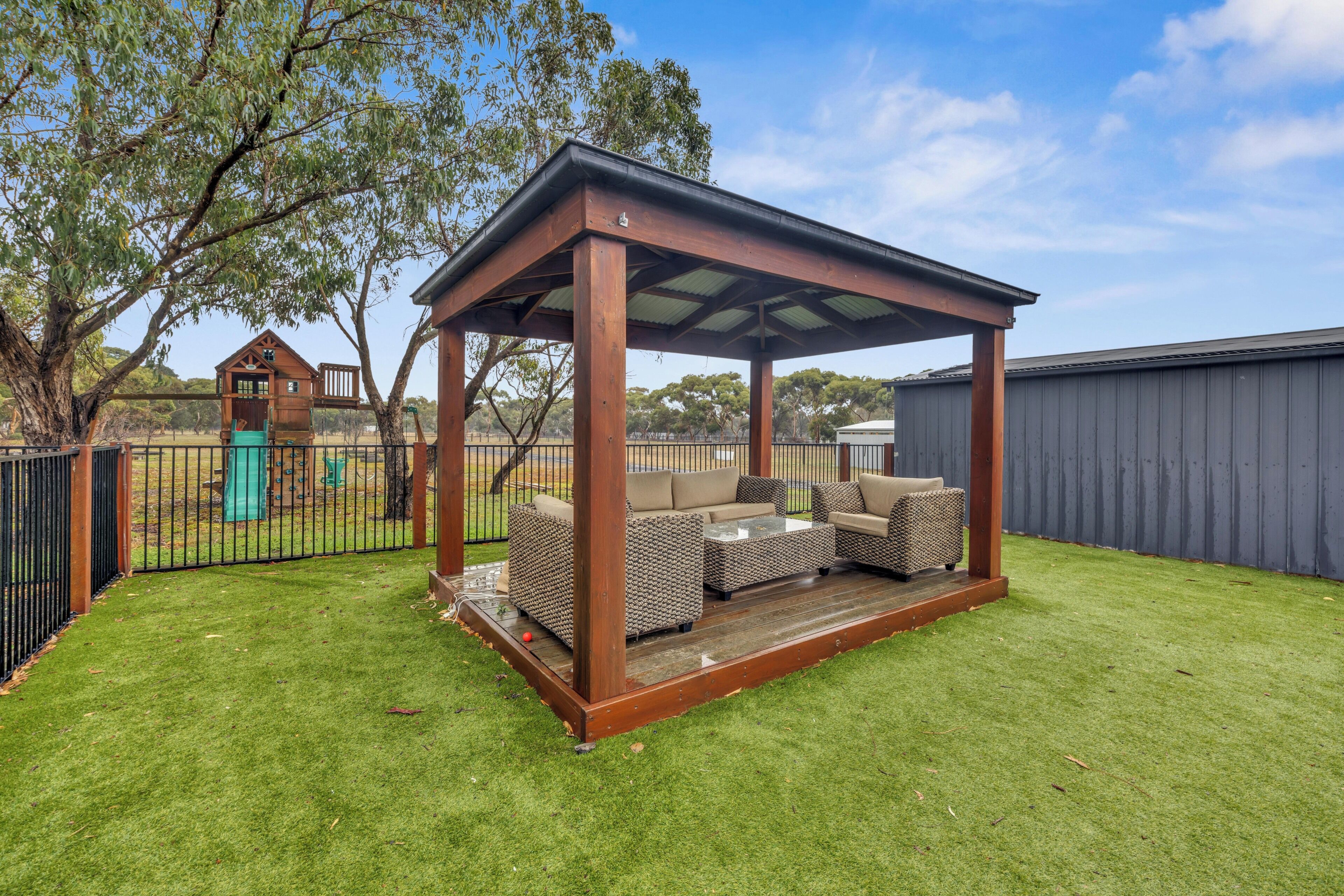 A covered outdoor seating area with a wooden structure, a table, and two sofas.