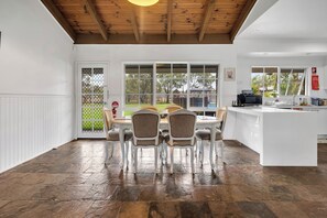 Un comedor amplio con una gran mesa y sillas, una isla de cocina y vistas a través de ventanas grandes.