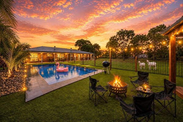 A backyard with a swimming pool, a flamingo float, a fire pit, and outdoor seating.