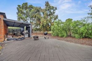 A patio area with a barbecue grill, a covered seating area, and a brick wall.