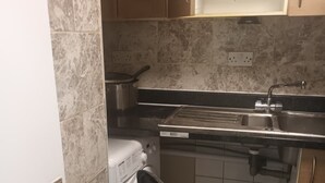 A compact kitchen with a washing machine, a stainless steel trash bin, and a pink bucket. - Beautiful 2-bedroom apartment in London perfect for your stay (London)