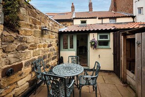 A stone wall, a metal table with chairs, and a building with a tiled roof. - Host & Stay | Hidden Winds Cottage (Guisborough)