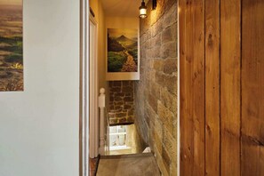 A hallway with a stone wall, wooden paneling, a hanging light fixture, and a framed landscape painting. - Host & Stay | Hidden Winds Cottage (Guisborough)