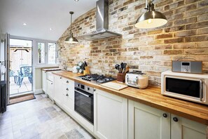 A kitchen with a brick wall, wooden countertop, stainless steel appliances, and a view to the outside. - Host & Stay | Hidden Winds Cottage (Guisborough)
