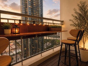 A balcony with a wooden railing, a small table with plants, a candle, and two chairs. - Marvelous 3-bedroom condo with AC in Thành phố Hồ Chí Minh (Thành phố Hồ Chí Minh)