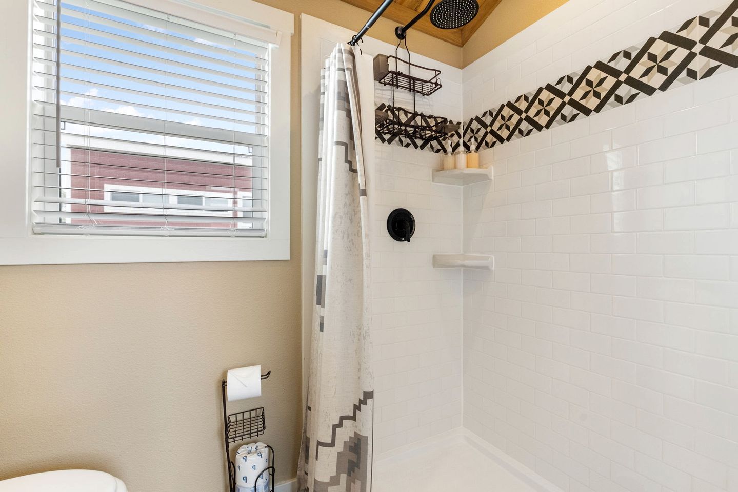 Une salle de bain avec une douche, une fenêtre avec des stores et un porte-serviettes.
