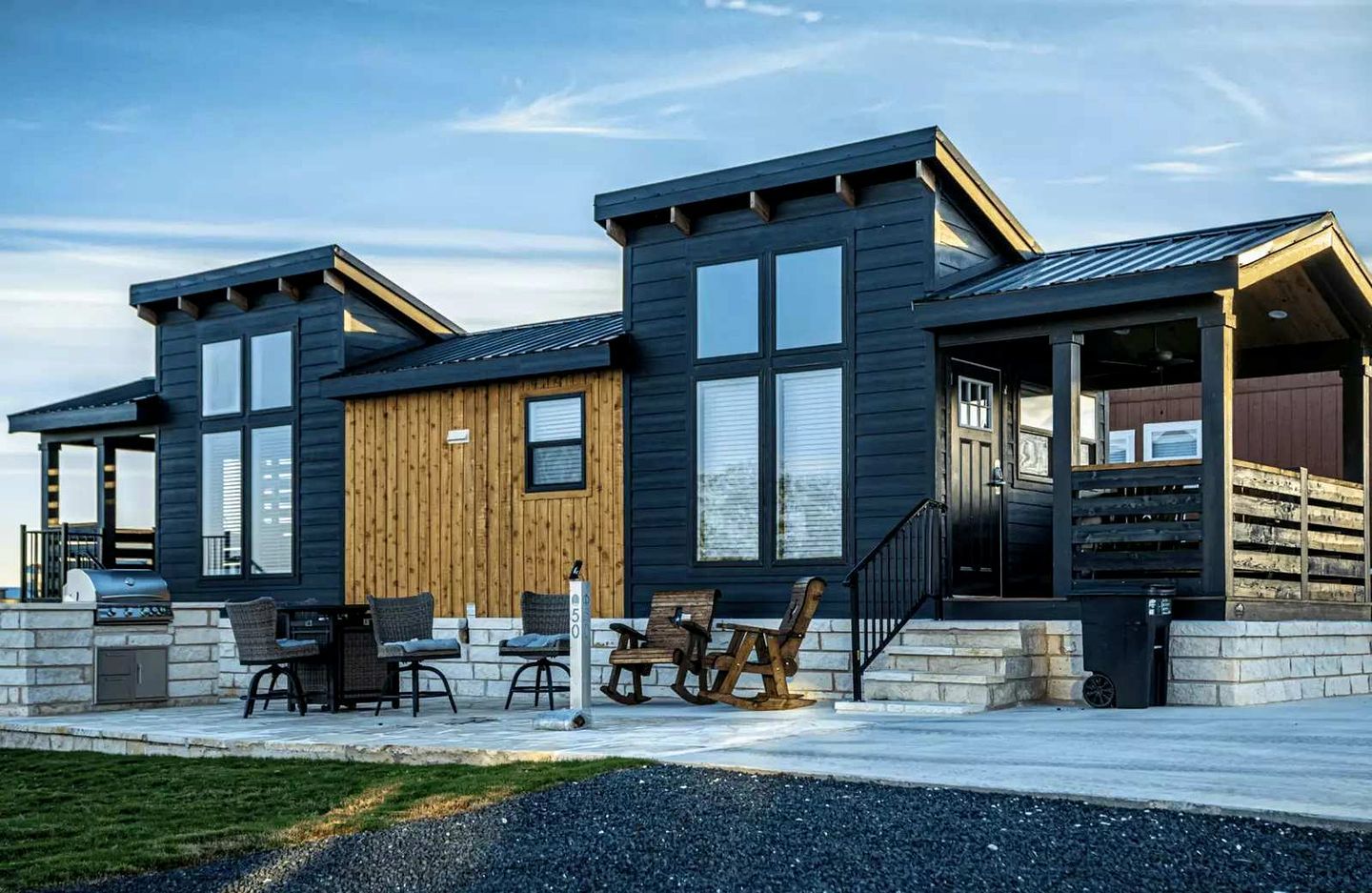 Een modern huis met twee verdiepingen, een stenen fundering, grote ramen en een houten accentmuur.