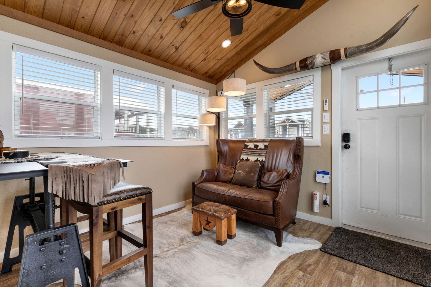 A room with a wooden ceiling, a leather sofa, a dining table with chairs, and a large door with a horn decoration.