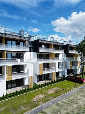 Un immeuble résidentiel moderne à plusieurs étages, doté de balcons, d’une cour intérieure et d’une voiture rouge garée dans l’allée.