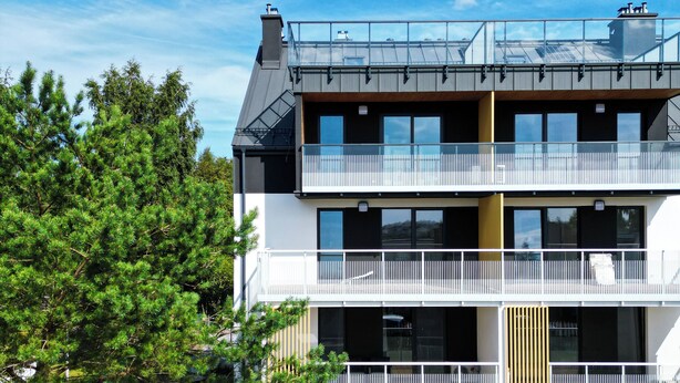 En modern tvåvåningsbyggnad med ett platt tak, stora fönster och en täckt uteplats.