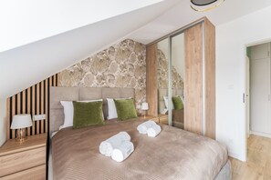 A modern bedroom with a sloped ceiling, a large bed with a headboard, and a mirror reflecting the room. - Posesja Plażowa Penthouse II & SPA (Grzybowo)