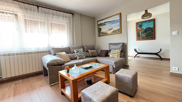 A living room with a sofa set, a coffee table, and two ottomans. There are two paintings on the wall.