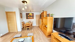 A modern living room with a wooden dining table, a glass-top coffee table, a built-in TV, and a bookshelf.