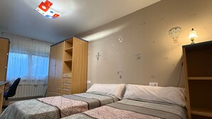 A bedroom with two beds, a desk, and a wardrobe.