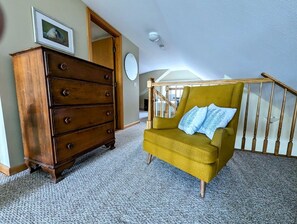 A room with a wooden dresser, a mustard-colored armchair with a blue pillow, and a staircase with wooden railings. - Oceanfront Cottage with Fire Pit & Direct Water Access Near Acadia National Park in Hancock, Maine (Hancock)