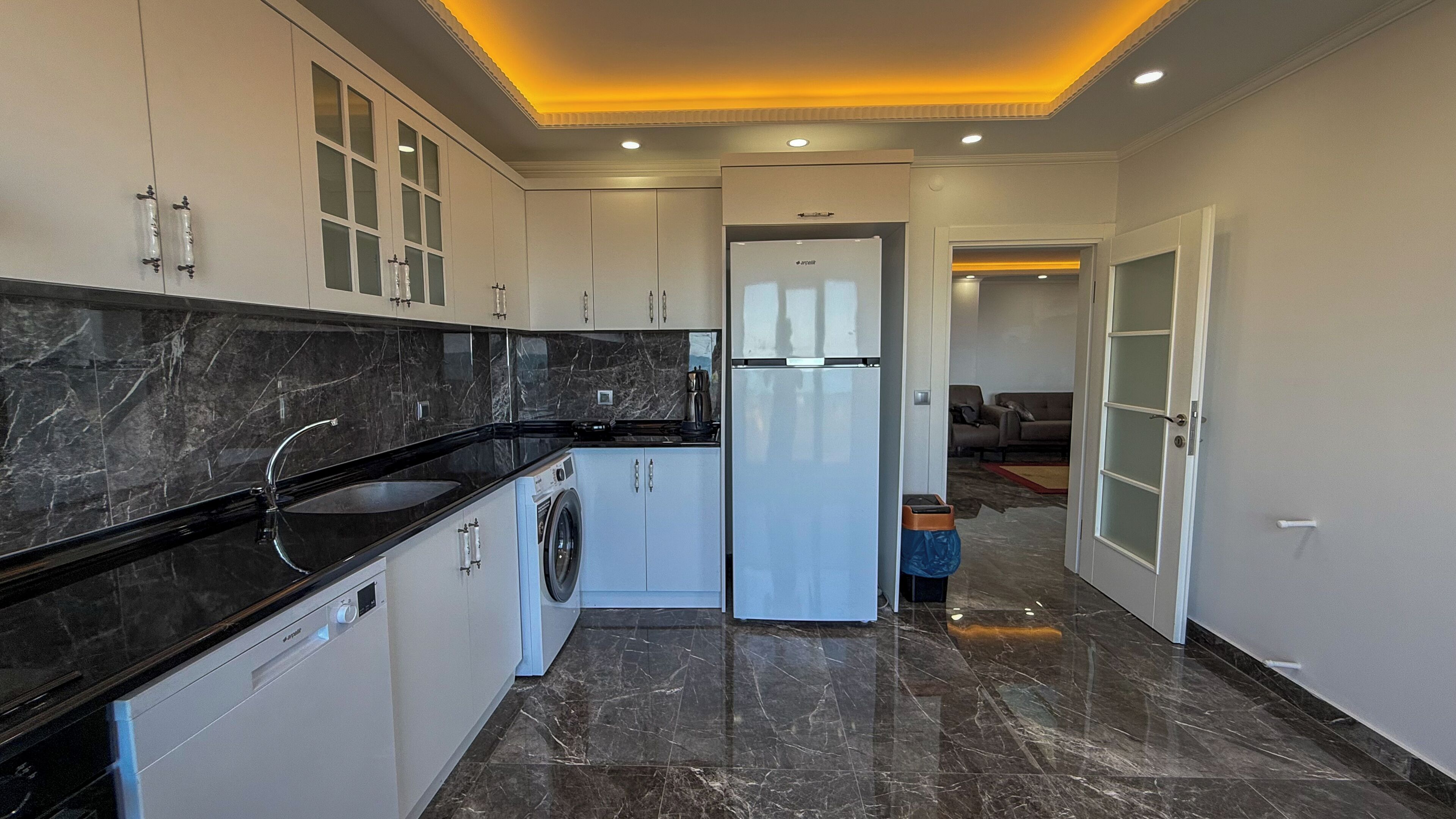 A modern kitchen with a built-in washing machine, a refrigerator, and a dining area with a sofa.