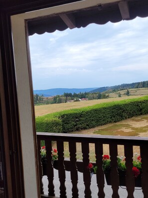 Blick von einem Balkon mit Geländer auf eine Landschaft mit Feldern und fernen Hügeln.