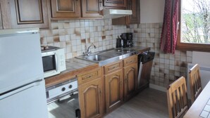 A kitchen with wooden cabinets, a microwave, a stove, a sink, and a window with curtains. - A peaceful mountain chalet at an elevation of 800 meters (Sapois)