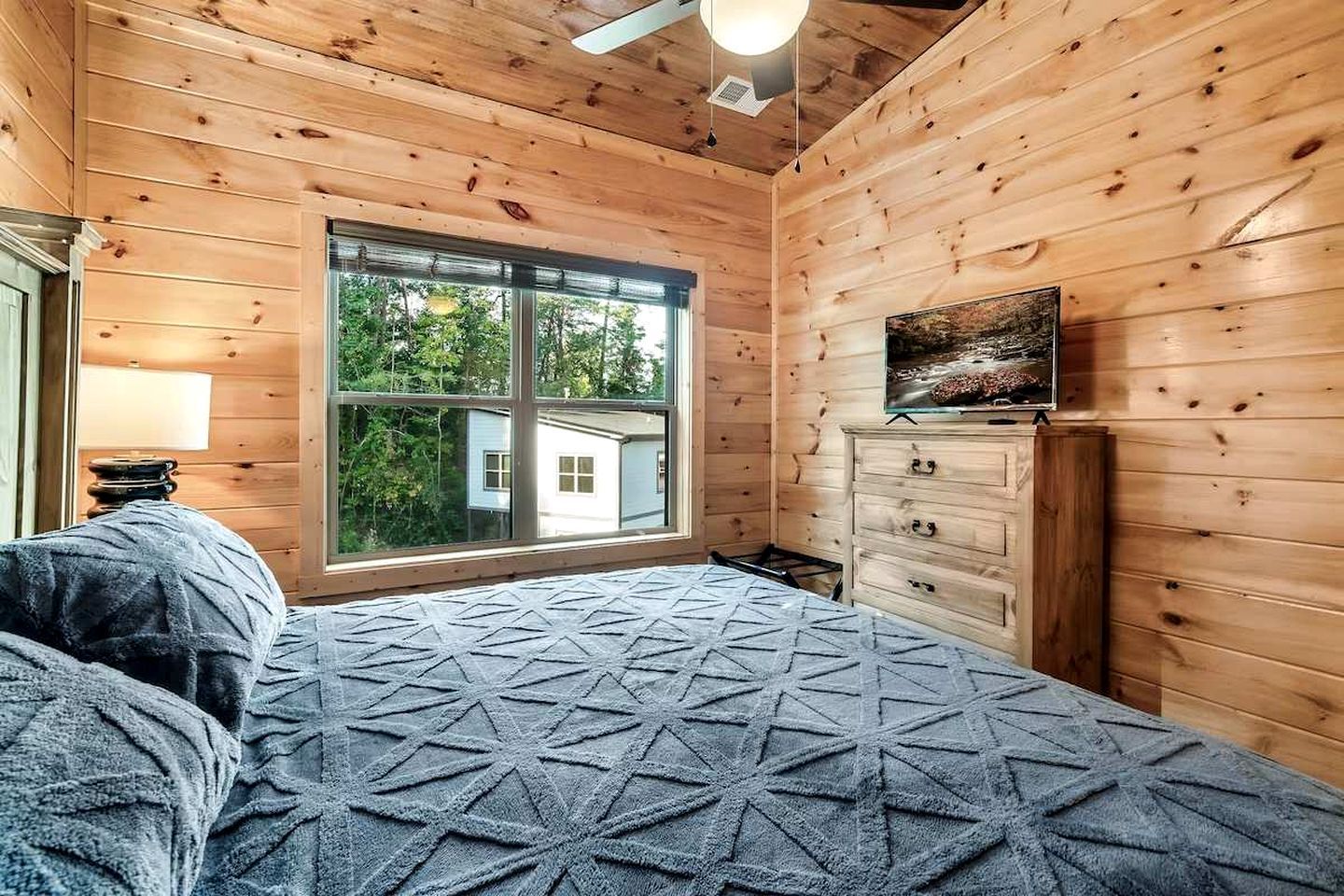Una habitación con una cama, un tocador, televisión y un ventanal grande.