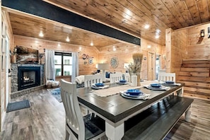A wooden interior with a dining table set for four, a fireplace, and a window. - Modern Cabin Retreat with Hot Tub & Game Loft in Pigeon Force, Tennessee (Pigeon Forge)