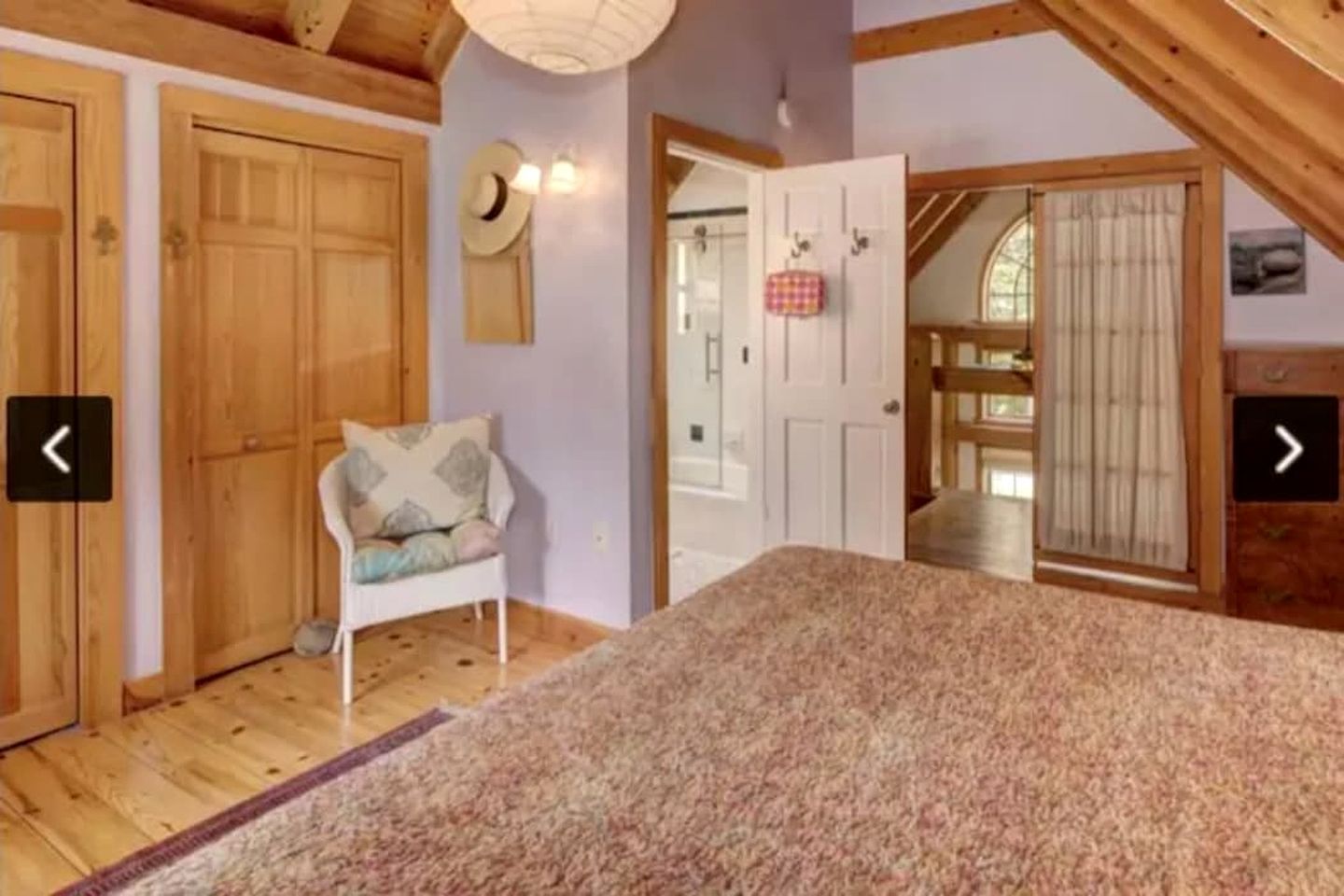 A room with a bed, a chair, wooden doors, and a view of another room.