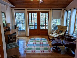 Ein gemütliches Zimmer mit Holzboden, einem karierten Teppich, einem Esstisch mit Stühlen, einem gepolsterten Sessel und einem Fenster mit Vorhängen.
