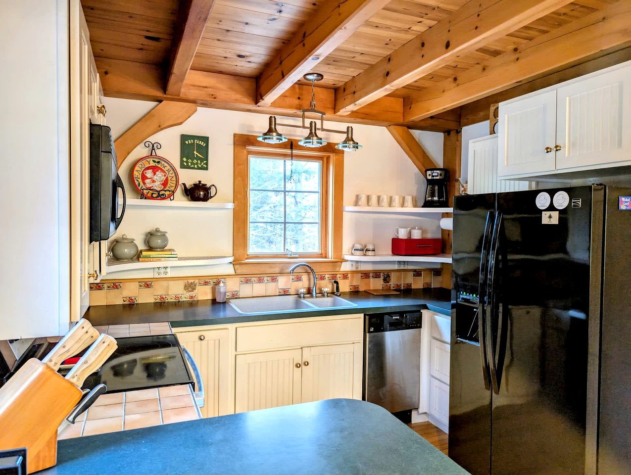 A kitchen with wooden beams, a black refrigerator, a sink, and a window.
