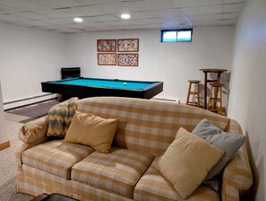 Ein Billardtisch in einem Raum mit einem karierten Sofa und einem Fenster.