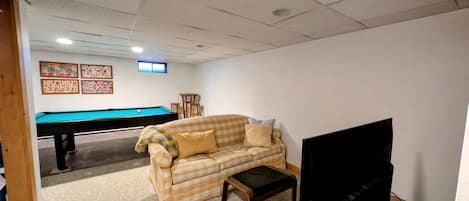A room with a pool table, a sofa, a television, and a ceiling with recessed lighting.
