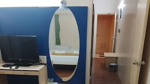 A hotel room with a bed, a desk with a computer, a mirror, and a bathroom visible through an open door. - Hotel De Rajnigandha (Nashik)