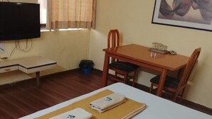A hotel room with a bed, a desk, a chair, a television, and a painting on the wall. - Hotel De Rajnigandha (Nashik)