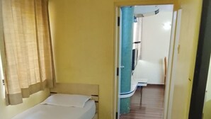 A room with a bed, a chair, and a desk. There is a door leading to another room. - Hotel De Rajnigandha (Nashik)