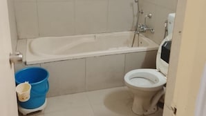 A bathroom with a bathtub, toilet, and a blue bucket. - Hotel De Rajnigandha (Nashik)