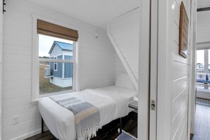 Ein kleines, weißes Zimmer mit einem Einzelbett und einem Fenster mit Blick auf ein blaues Haus.
